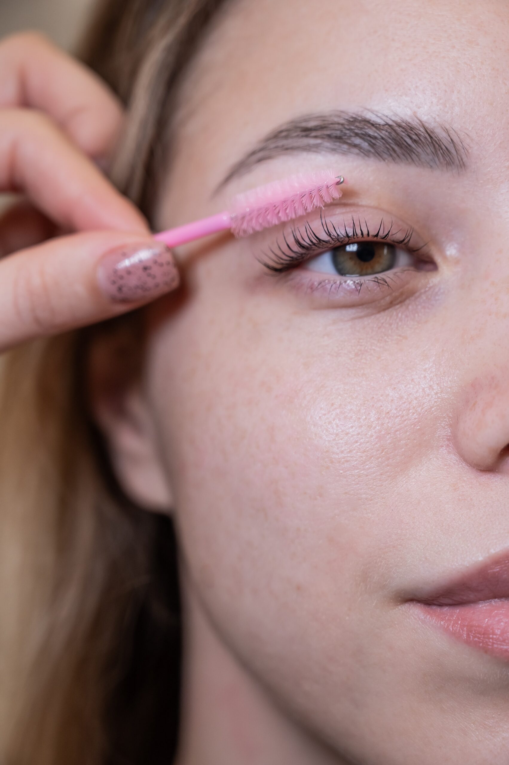 Caucasian woman brushing her eyelashes after lamination.